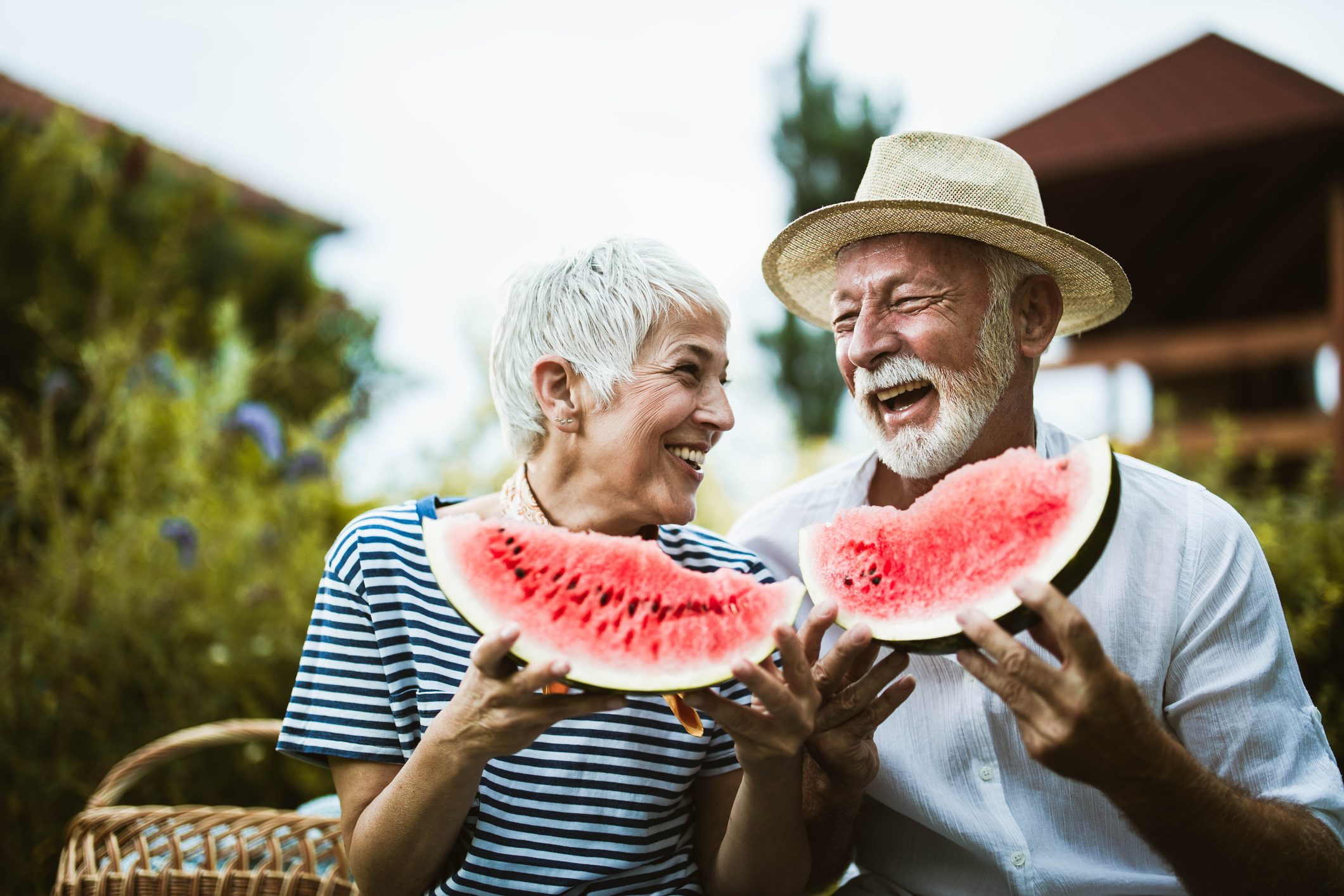 Cheerful mature couple having fun while eating watermelon during picnic day in nature.